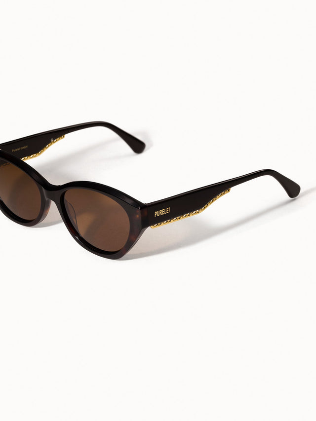 Lagoon Sonnenbrille in dunkelbraunem Acetat mit ovaler Form, goldener Verzierung und PURELEI Logo, elegant und modern.