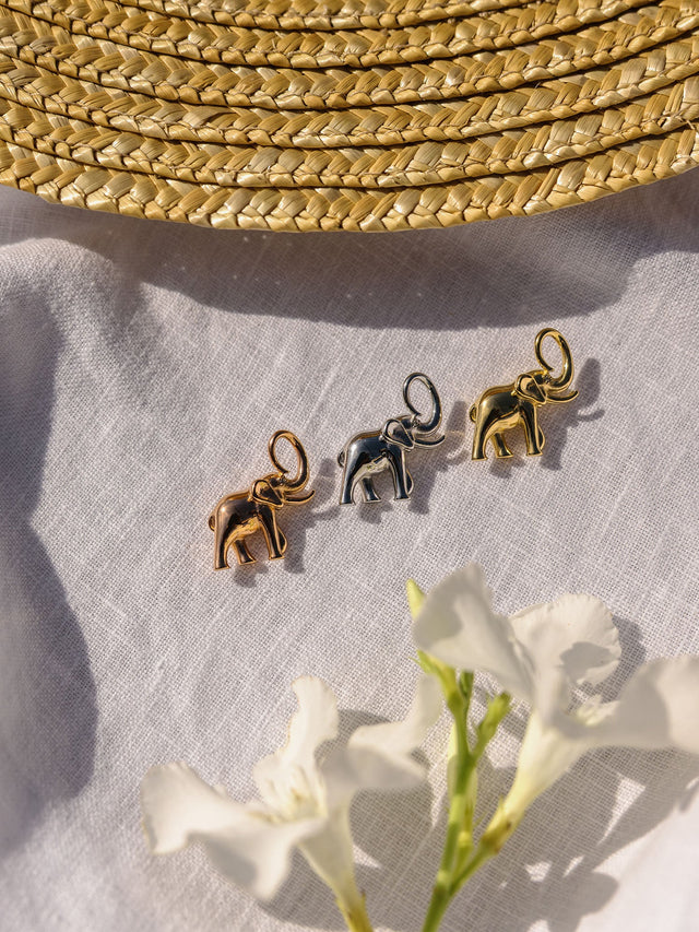 Drei PURELEI Flowing Strength Elefant Charms in Gold, Silber und Roségold auf Leinen in warmem Sonnenlicht.