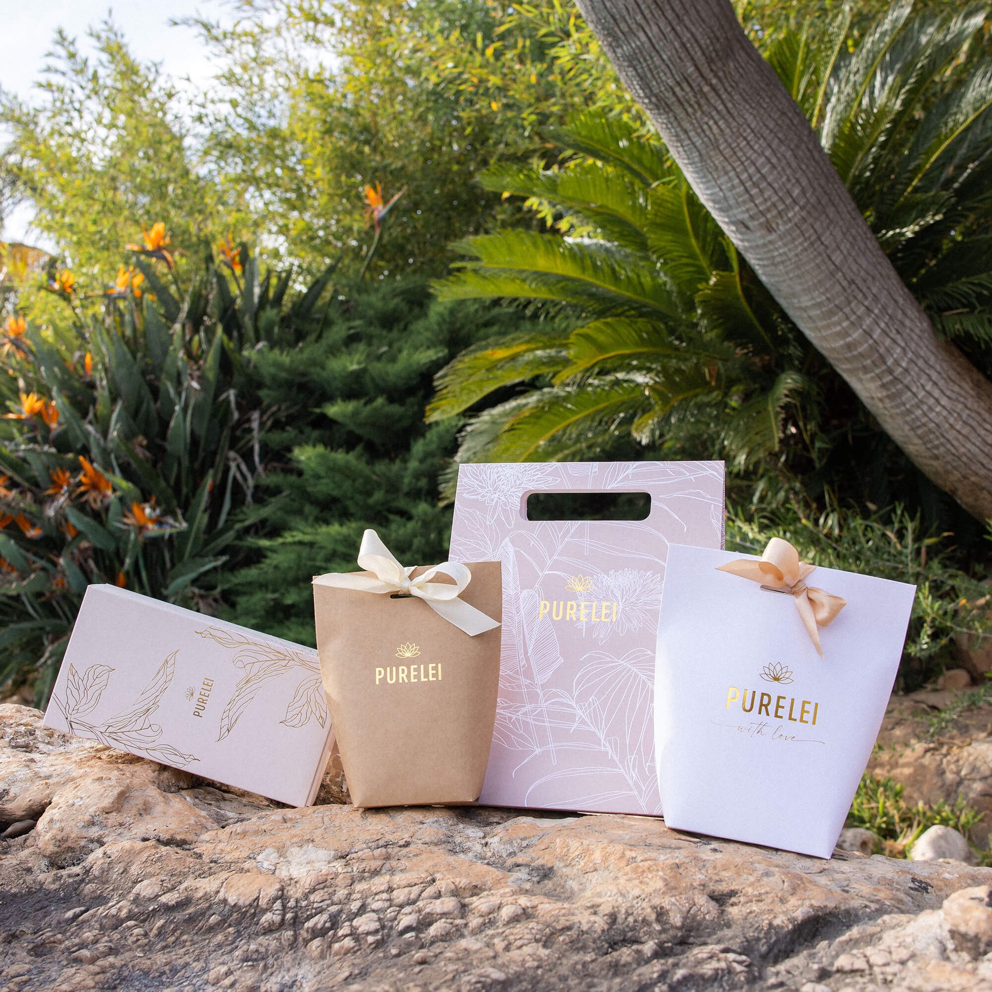 Elegante PURELEI Geschenkverpackungen in Gold und Weiß, umgeben von tropischer Natur.