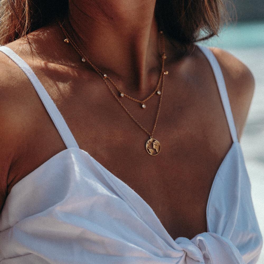 PURELEI World Map Kette aus goldfarbenem Edelstahl, filigran getragen, strahlt sommerliche Leichtigkeit und Abenteuerlust aus.