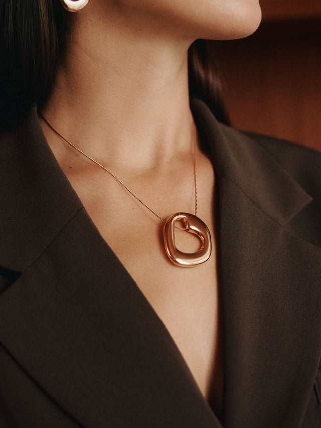 Braune, elegante PURELEI Halskette mit geschwungenem Anhänger, getragen in stilvollem Outfit.