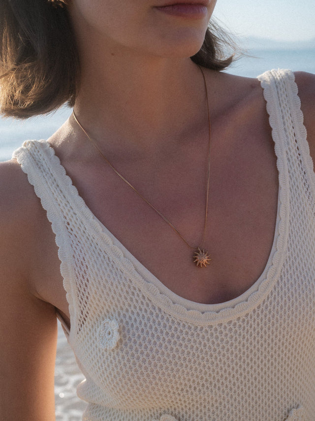 Goldene PURELEI Kette mit Sonnenanhänger, getragen in natürlicher Lichtstimmung am Strand.
