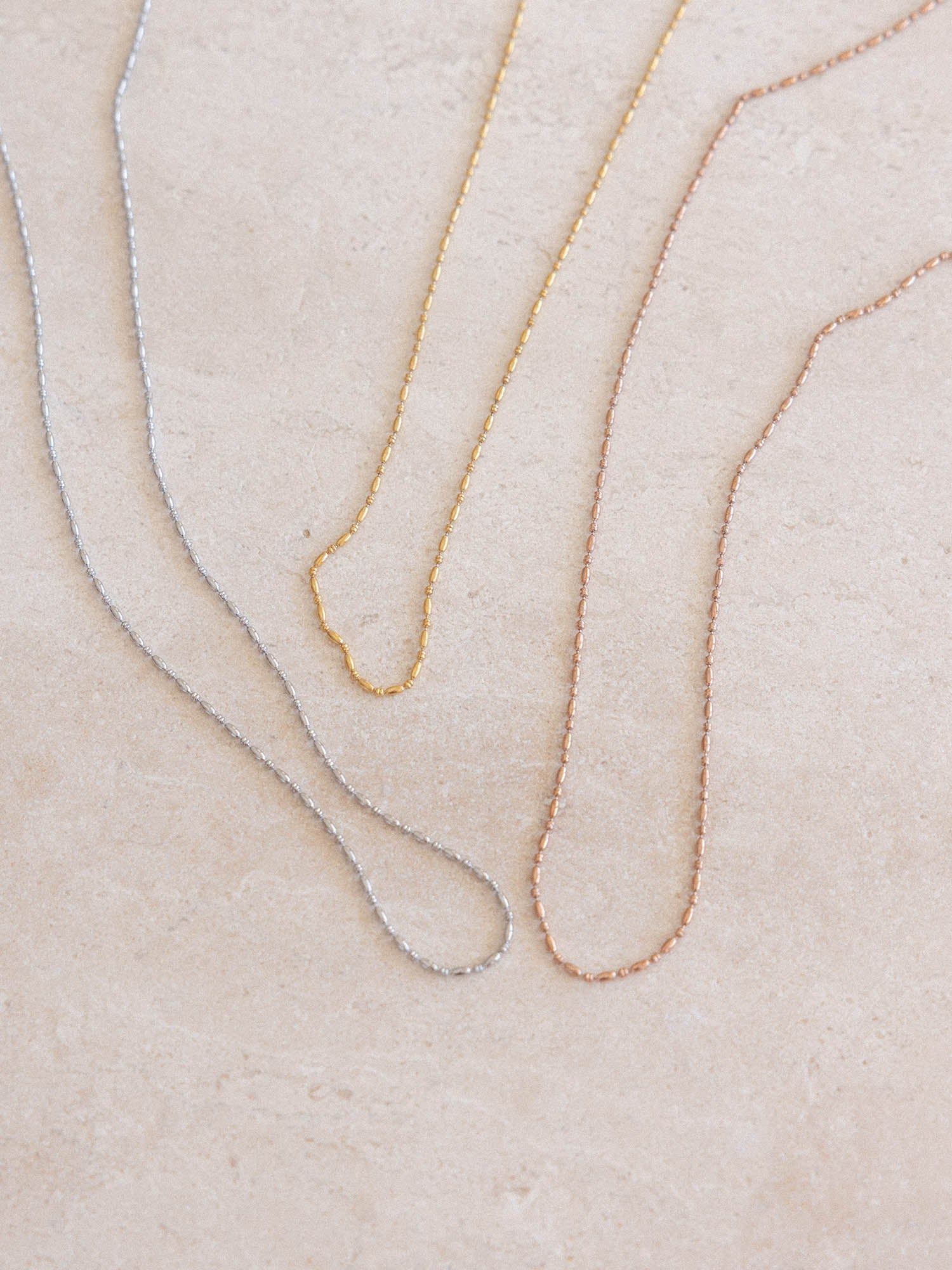 Moments Kette in Gold, Silber und Roségold mit perlenförmigen Kettengliedern auf hellem Stein, elegant und feminin von PURELEI.