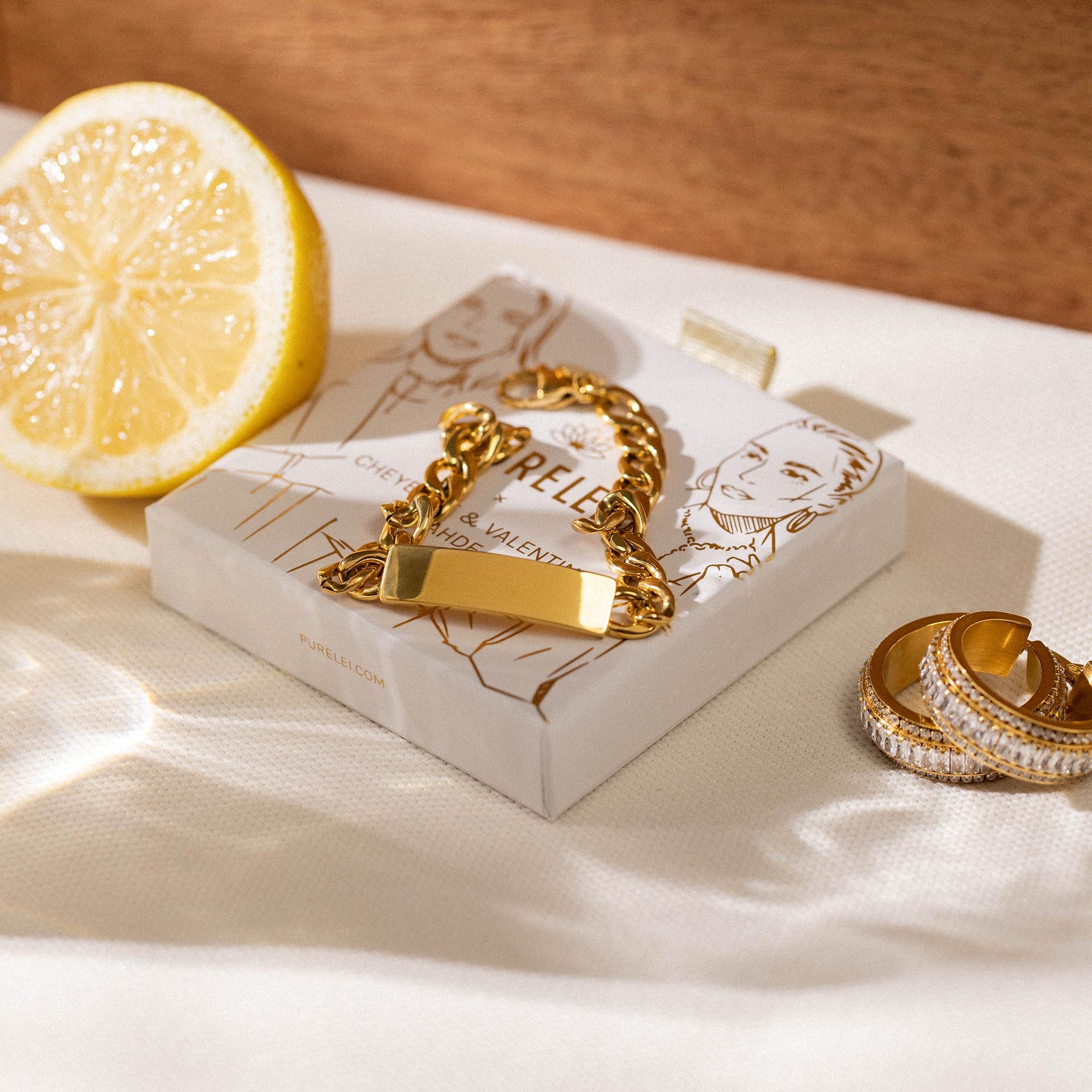 PURELEI Coco Armband aus 18K Gold, gravierbares Gliederarmband, warmes Licht, elegante Inszenierung auf Stoff.