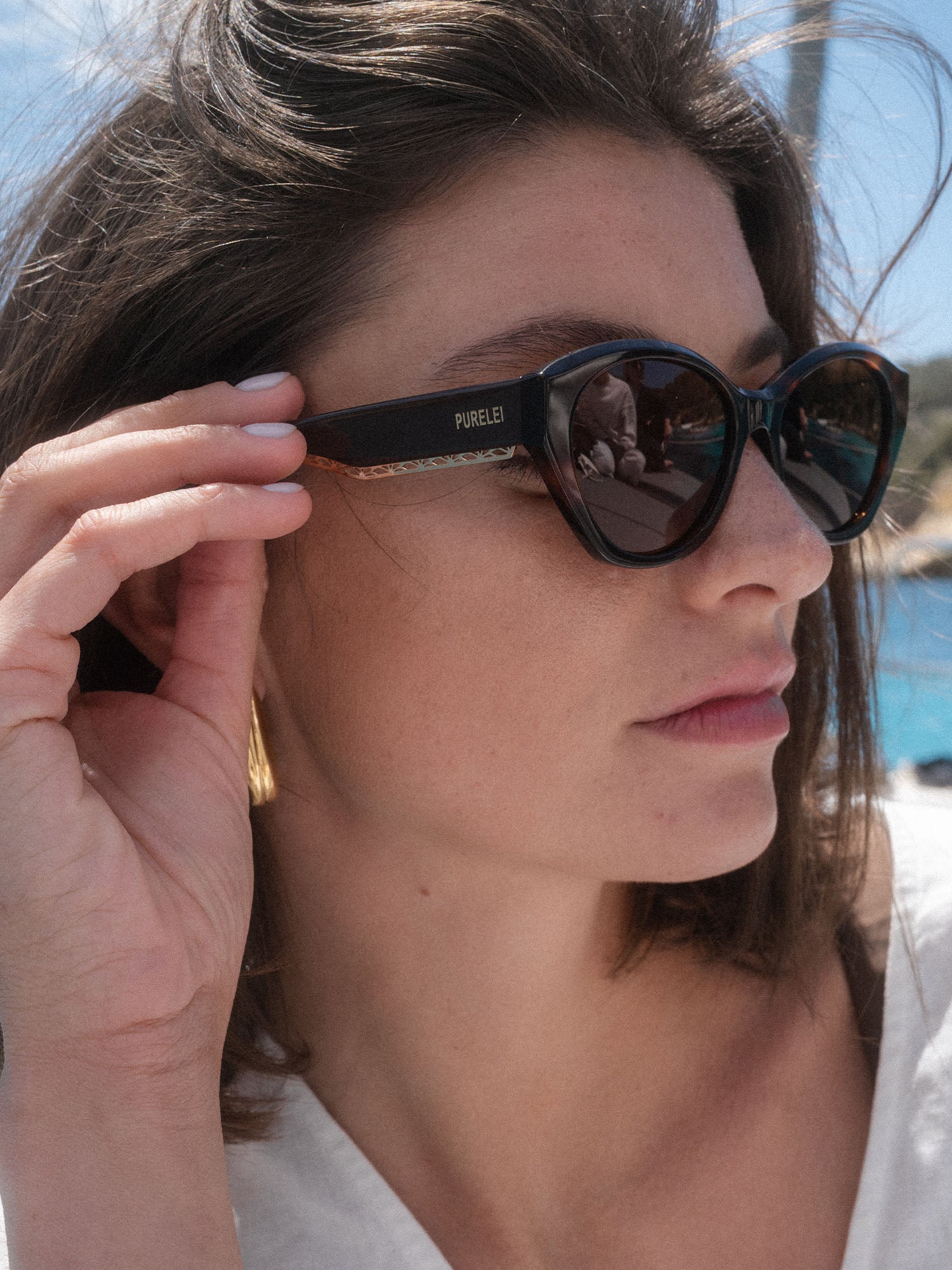Lagoon Sonnenbrille von PURELEI, oval, dunkelbraunes Acetat mit goldener Verzierung, modern und elegant am Strand getragen
