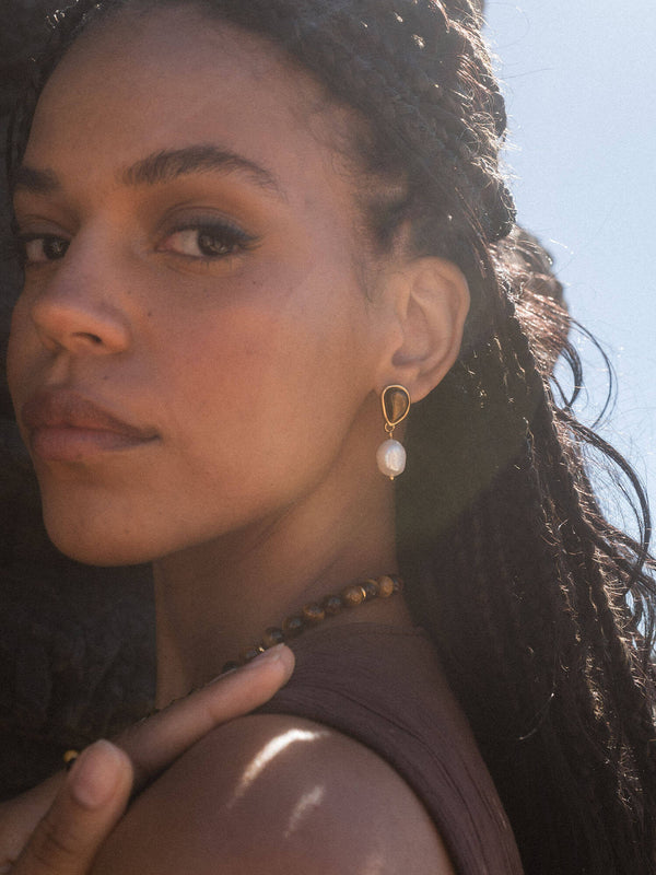 Elegante PURELEI Ohrringe mit Muschel-Anhänger, goldfarben, in warmem Licht getragen.